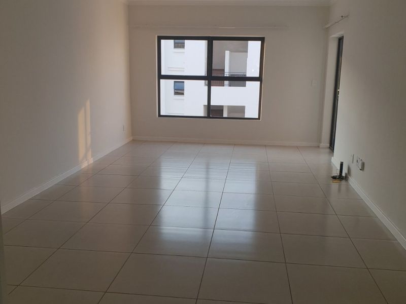 A bright, empty living room featuring neutral tiled flooring and a large window, providing a clean and versatile space ready for furnishing.