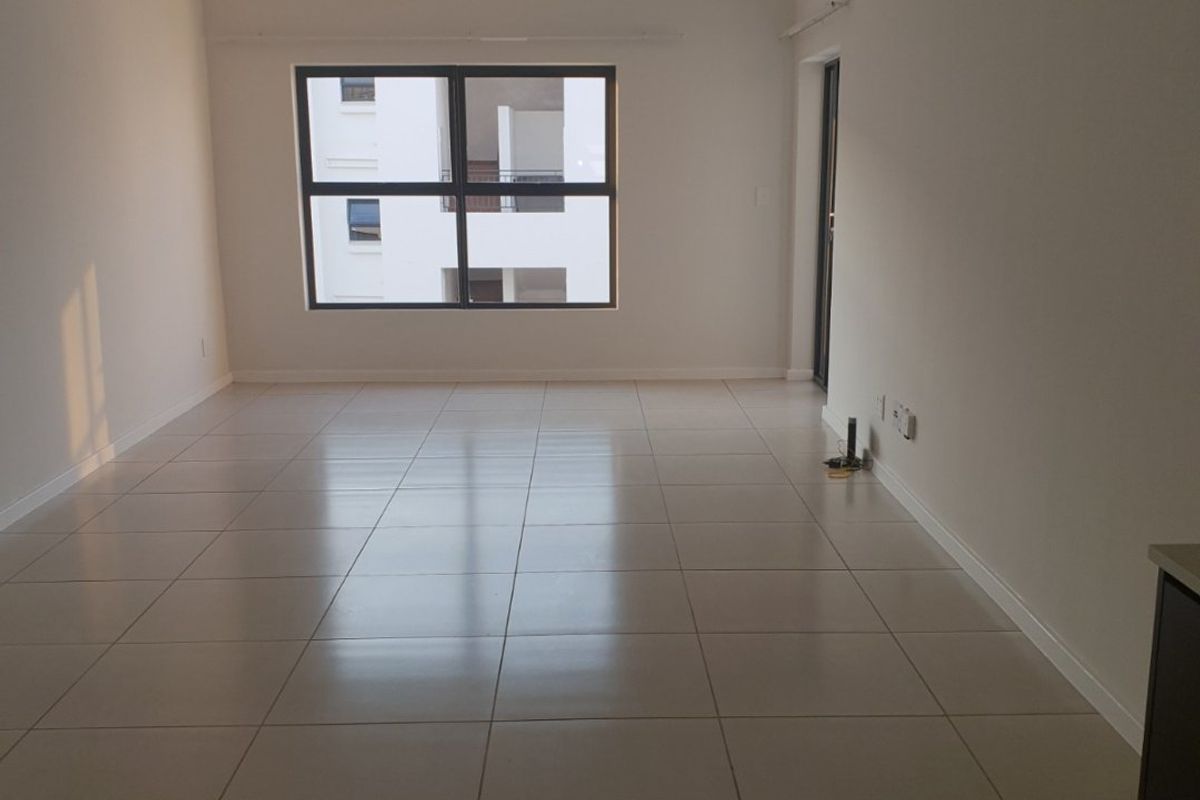 A bright, empty living area featuring neutral tiled flooring and large aluminium-framed windows, offering a clean and versatile space ready for furnishing.