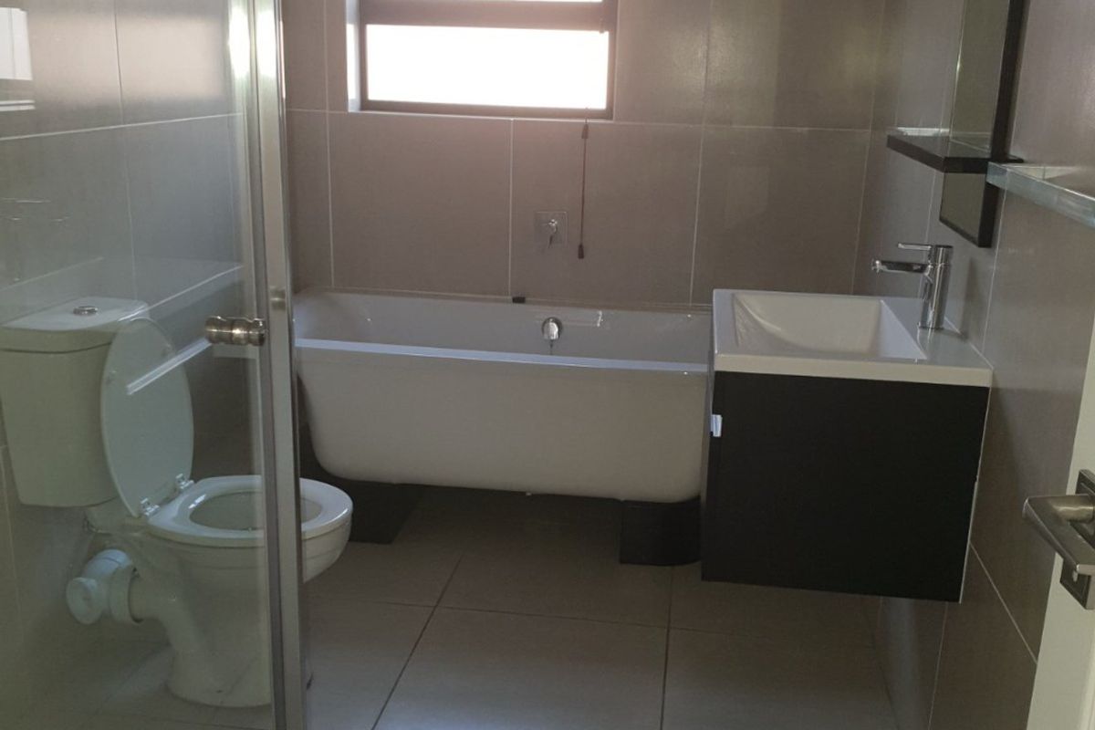 Modern bathroom featuring a freestanding bathtub, wall-mounted vanity, glass shower enclosure, and neutral floor-to-ceiling tiling.