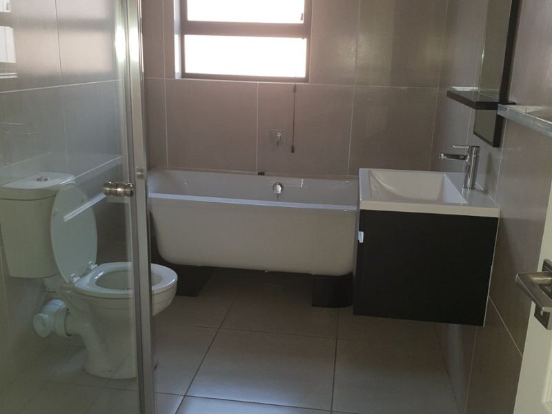 Modern bathroom featuring a freestanding bathtub, wall-mounted vanity, glass shower enclosure, and neutral floor-to-ceiling tiling.