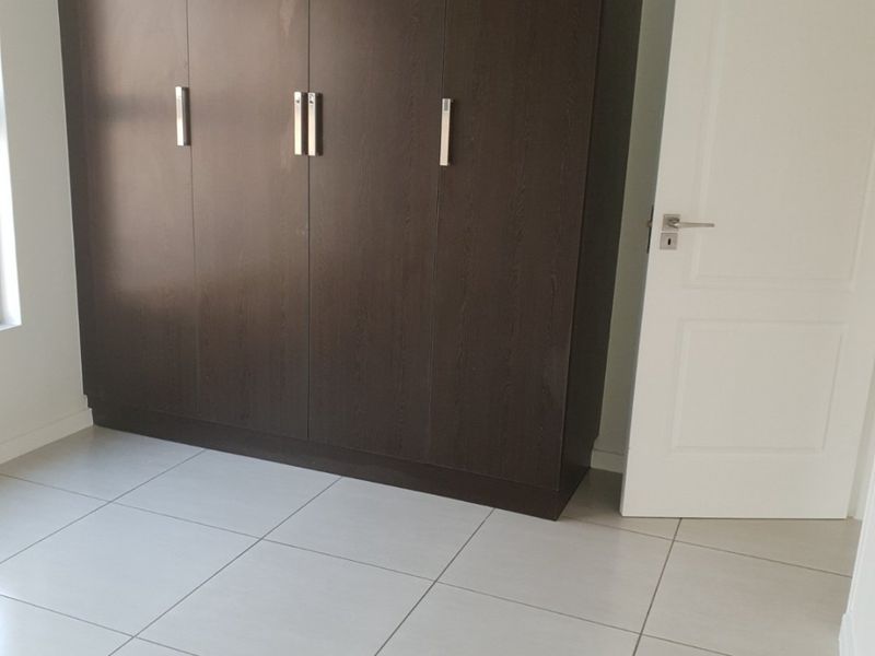 A clean, empty bedroom featuring modern dark wood built-in cupboards and neutral light-colored floor tiles.