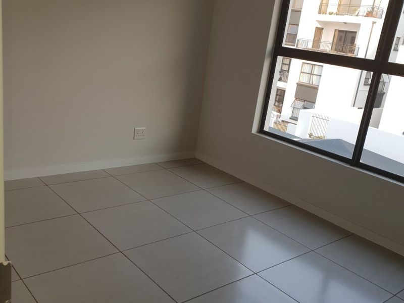A bright, empty bedroom featuring neutral tiled flooring and a large window providing natural light and an exterior view.