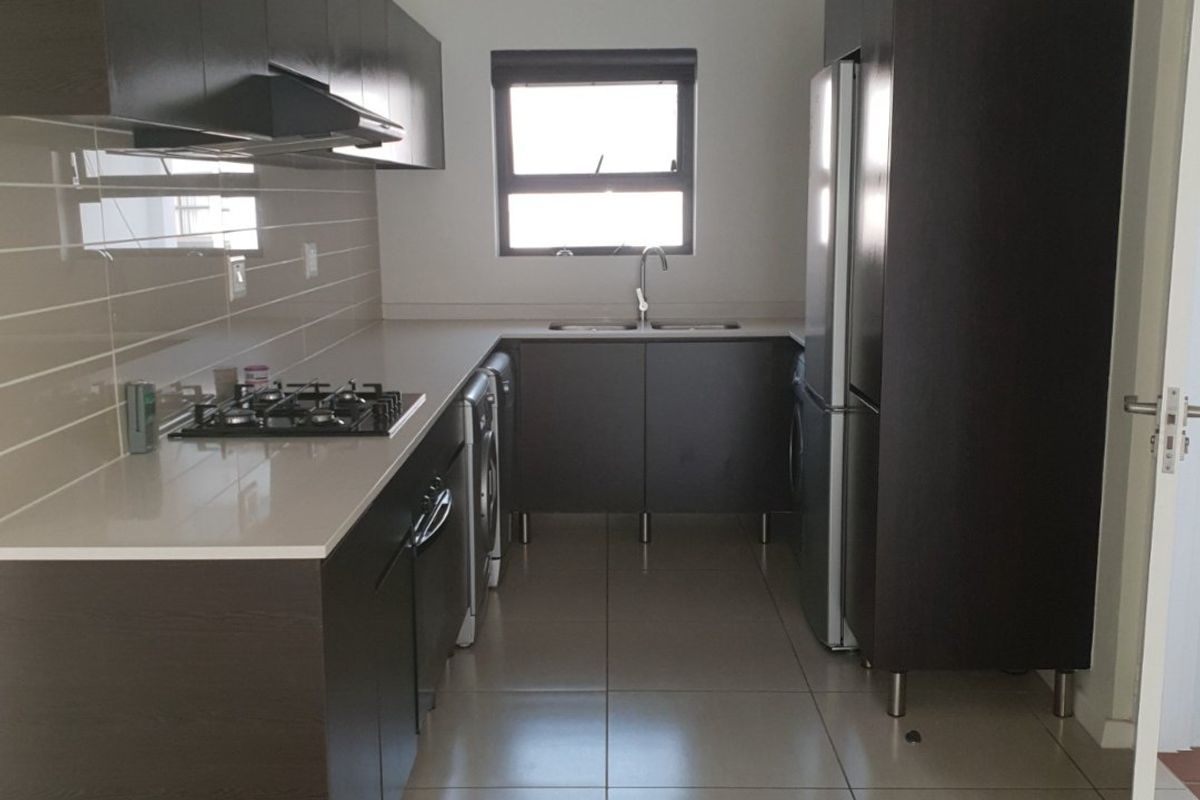 A functional kitchen featuring dark wood cabinetry, stone countertops, a gas hob with extractor fan, and tiled flooring throughout.