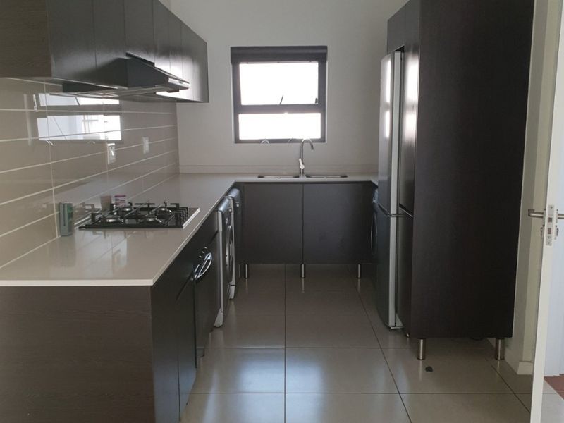 A functional kitchen featuring dark wood cabinetry, stone countertops, a gas hob with extractor fan, and tiled flooring throughout.