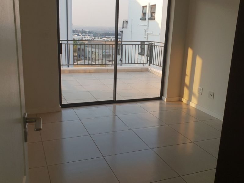 A bright, empty living area featuring neutral tiled flooring and a large sliding glass door that opens onto a private balcony with neighborhood views.