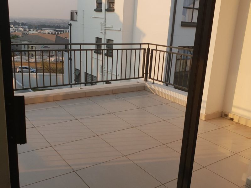 A clean, tiled balcony featuring a metal balustrade and sliding glass door access, offering an elevated view of the surrounding residential area.