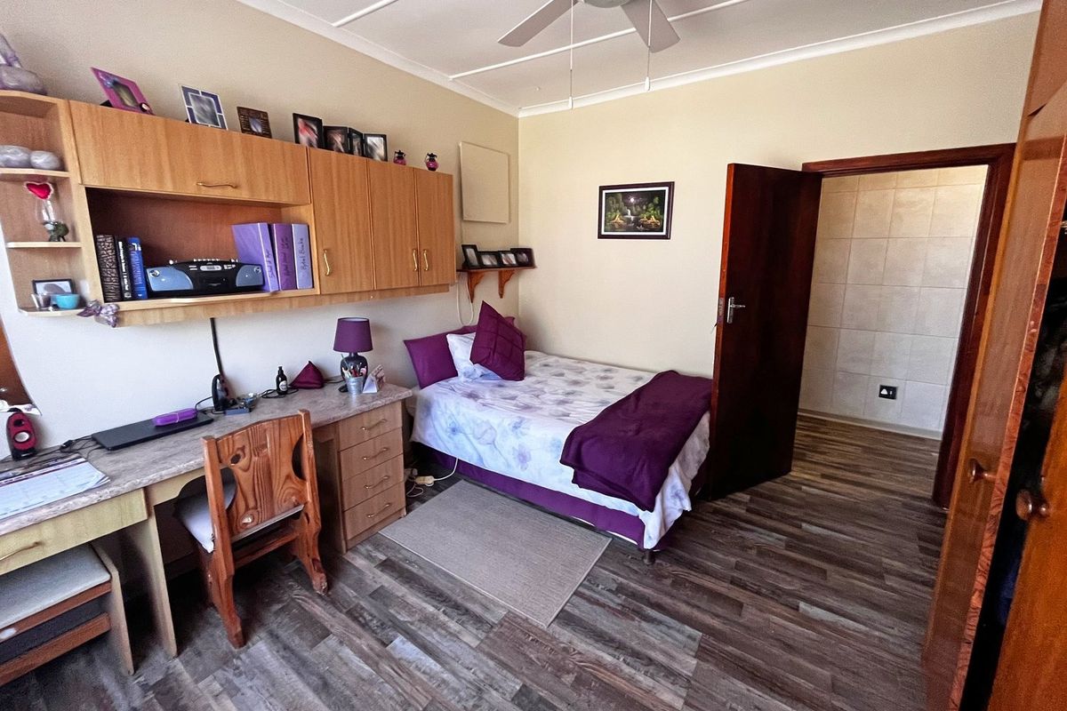 A functional bedroom featuring laminate flooring, a ceiling fan, and integrated built-in desk and cabinetry for storage.