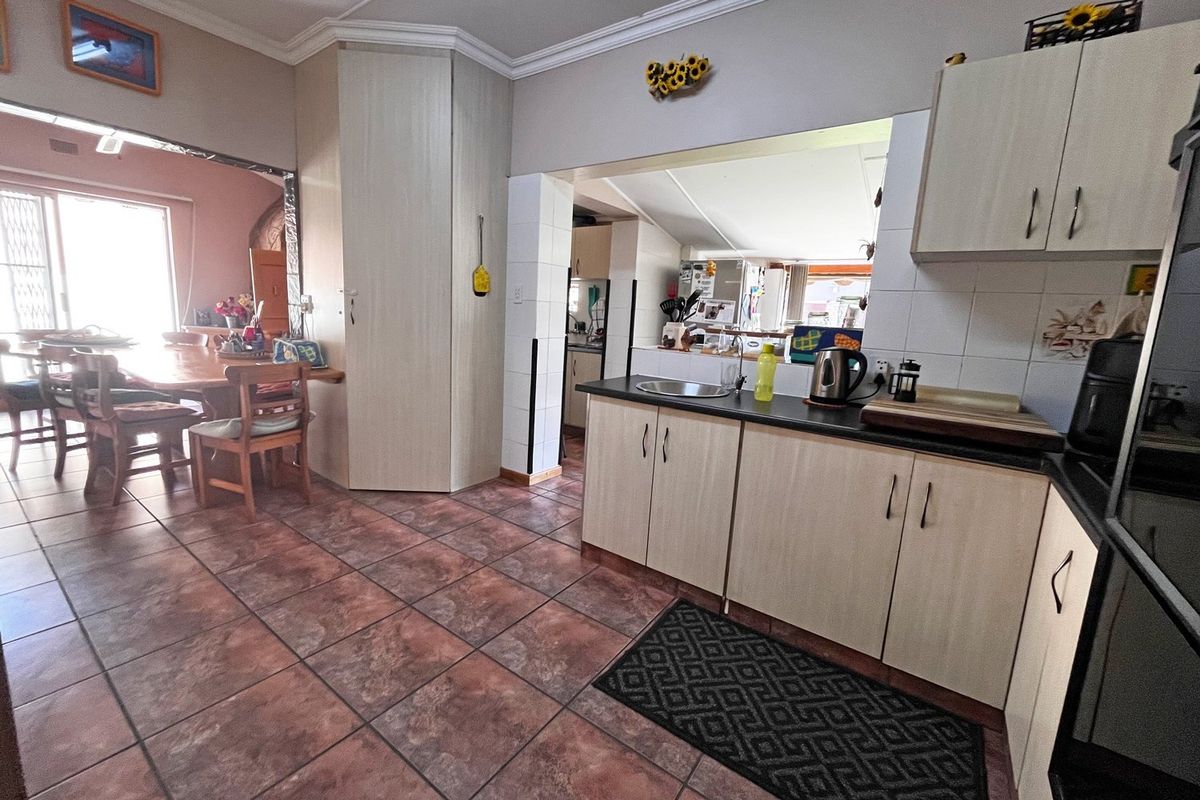 A functional kitchen featuring light-toned built-in cabinetry, dark laminate countertops, and tiled flooring, with an open-plan layout connecting to the adjacent dining area.