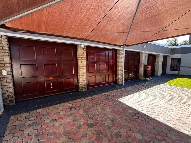 A triple garage featuring dark wood-finish doors, brick pillars, and a paved driveway area covered by a large shade sail.