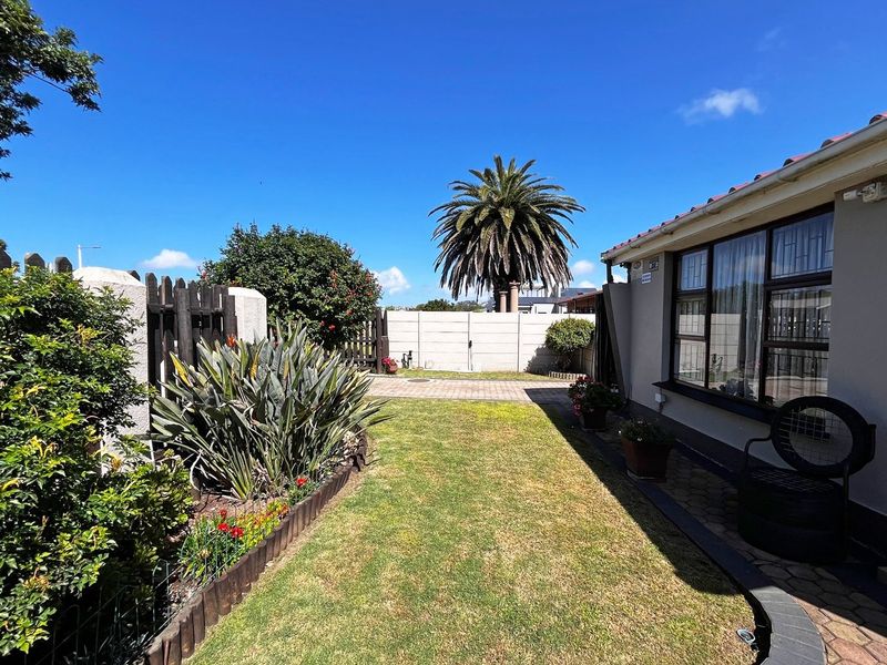 A well-maintained rear garden featuring a paved walkway, established landscaping, and secure boundary walling adjacent to the main dwelling.