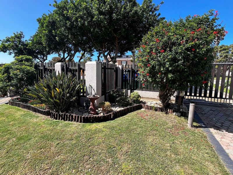 A well-maintained front garden featuring a timber picket fence, masonry pillars, and established landscaping with paved driveway access.