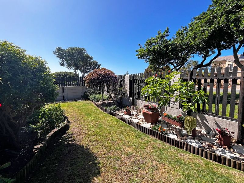 A well-maintained private garden featuring a manicured lawn, established trees, and a secure timber picket fence boundary.