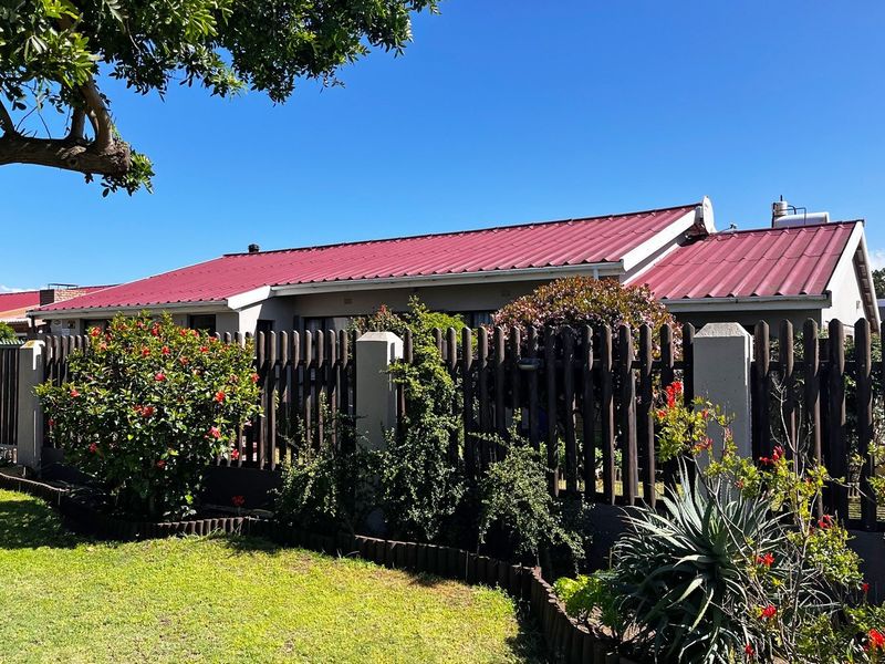 Front view of a residential house featuring a red corrugated metal roof, masonry pillars, and a timber picket fence surrounding a well-maintained garden.