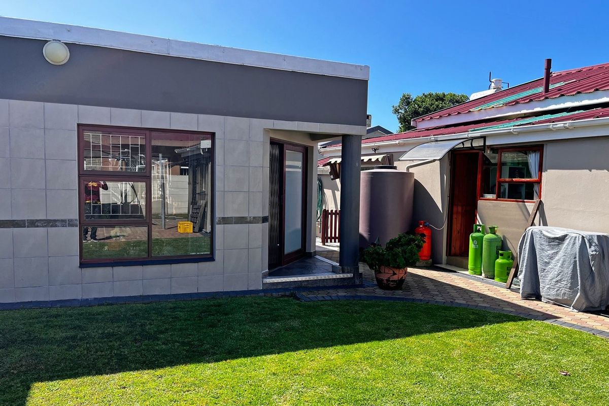 Rear exterior view of the property featuring a tiled facade, paved patio area, lawn, and integrated water storage tank.