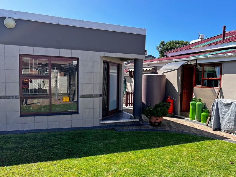 Rear exterior view of the property featuring a tiled facade, paved patio area, lawn, and integrated water storage tank.