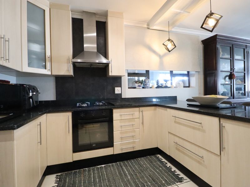 A well-maintained kitchen featuring light wood cabinetry, dark granite countertops, a built-in oven with gas hob, and modern pendant lighting.