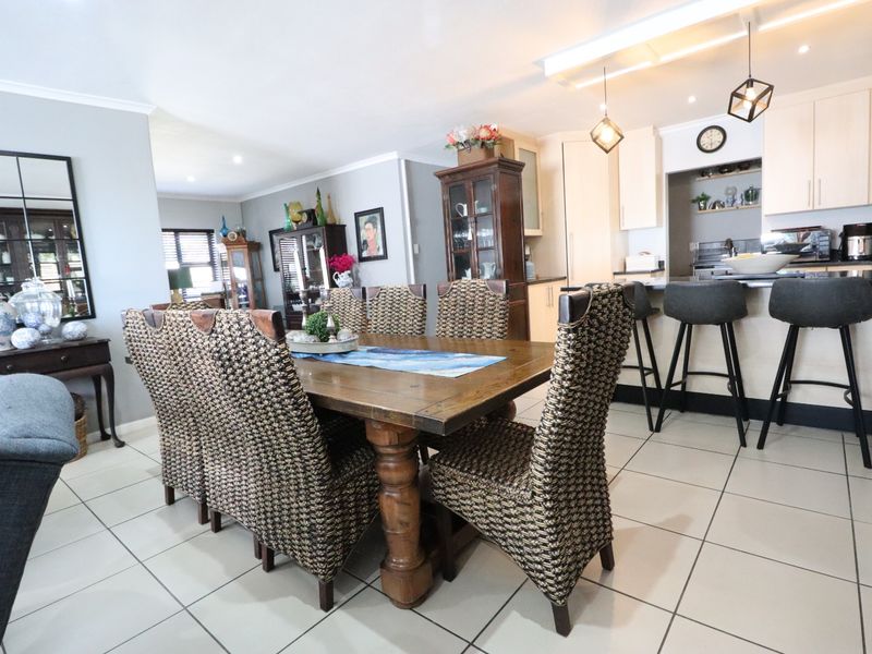 An open-plan living and dining area featuring a modern kitchen with a breakfast bar, stone countertops, and neutral tiled flooring throughout.