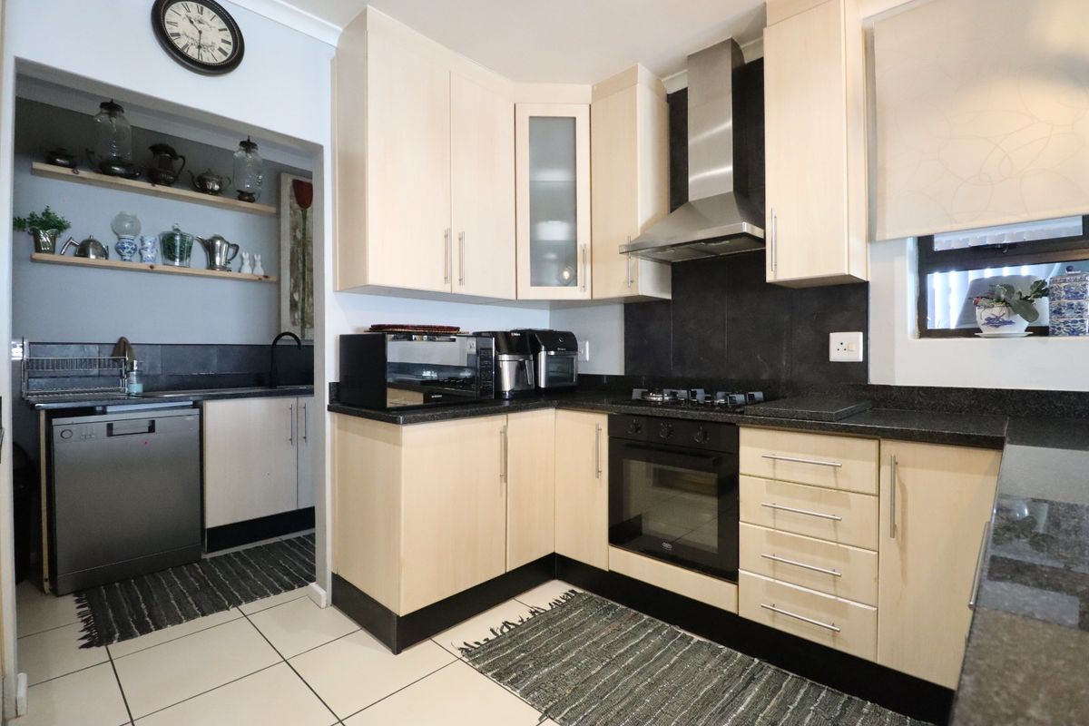 A functional kitchen featuring light wood cabinetry, dark granite countertops, a built-in oven with gas hob, and an adjacent scullery area.