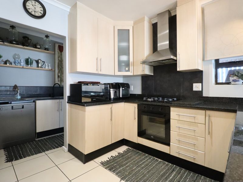 A functional kitchen featuring light wood cabinetry, dark granite countertops, a built-in oven with gas hob, and an adjacent scullery area.