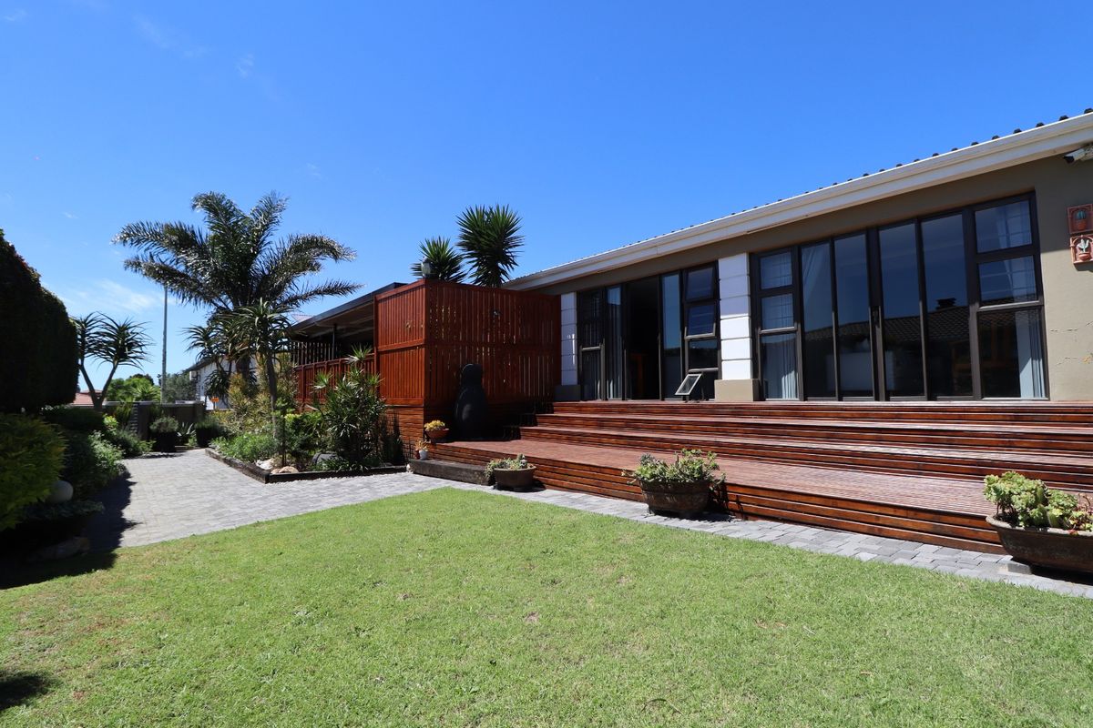 A well-maintained rear exterior featuring extensive timber decking, large sliding glass doors, and a landscaped garden with paved pathways.