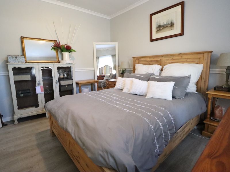 A well-maintained bedroom featuring light-toned laminate flooring, neutral wall paint, and classic coving details.