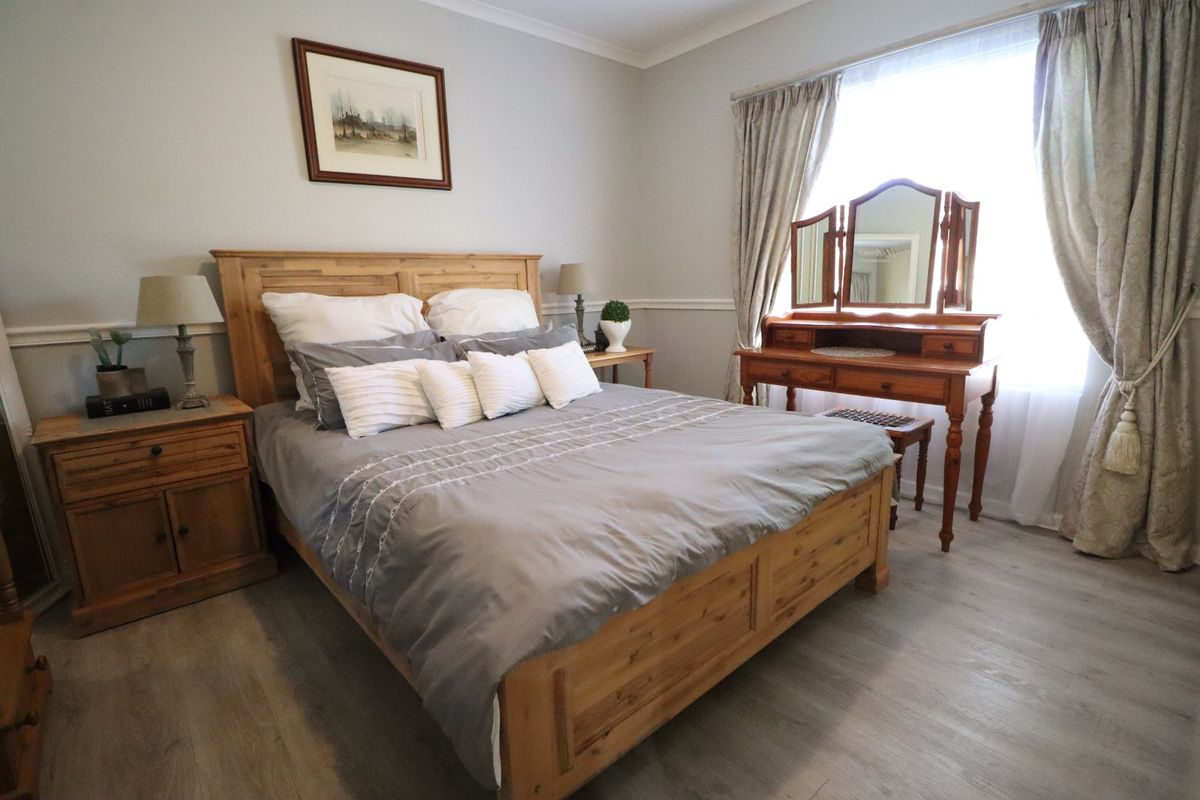 A well-maintained bedroom featuring light-toned laminate flooring, decorative chair rail molding, and classic coving, creating a comfortable and inviting living space.