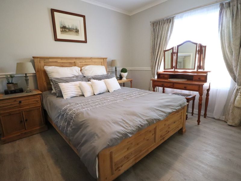 A well-maintained bedroom featuring light-toned laminate flooring, decorative chair rail molding, and classic coving, creating a comfortable and inviting living space.