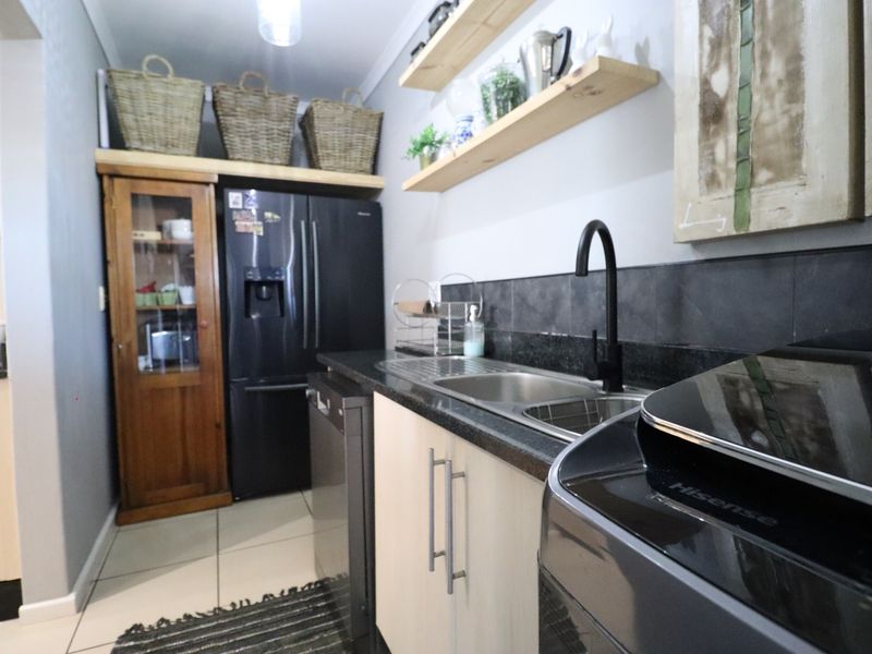 A functional scullery featuring modern cabinetry, stone countertops, a stainless steel sink with a black mixer tap, and open timber shelving.