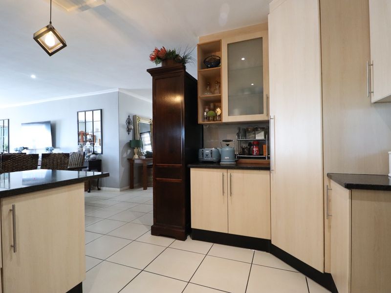 Open plan kitchen area featuring light wood cabinetry, dark granite countertops, and tiled flooring, seamlessly flowing into the adjacent living and dining space.