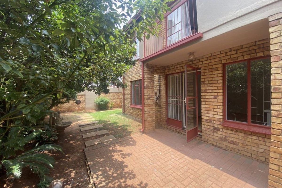 Rear view of the apartment featuring a brick facade, paved patio area, and a small balcony overlooking the garden.