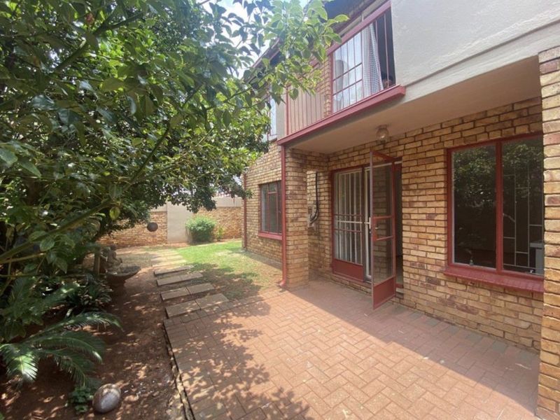 Rear view of the apartment featuring a brick facade, paved patio area, and a small balcony overlooking the garden.
