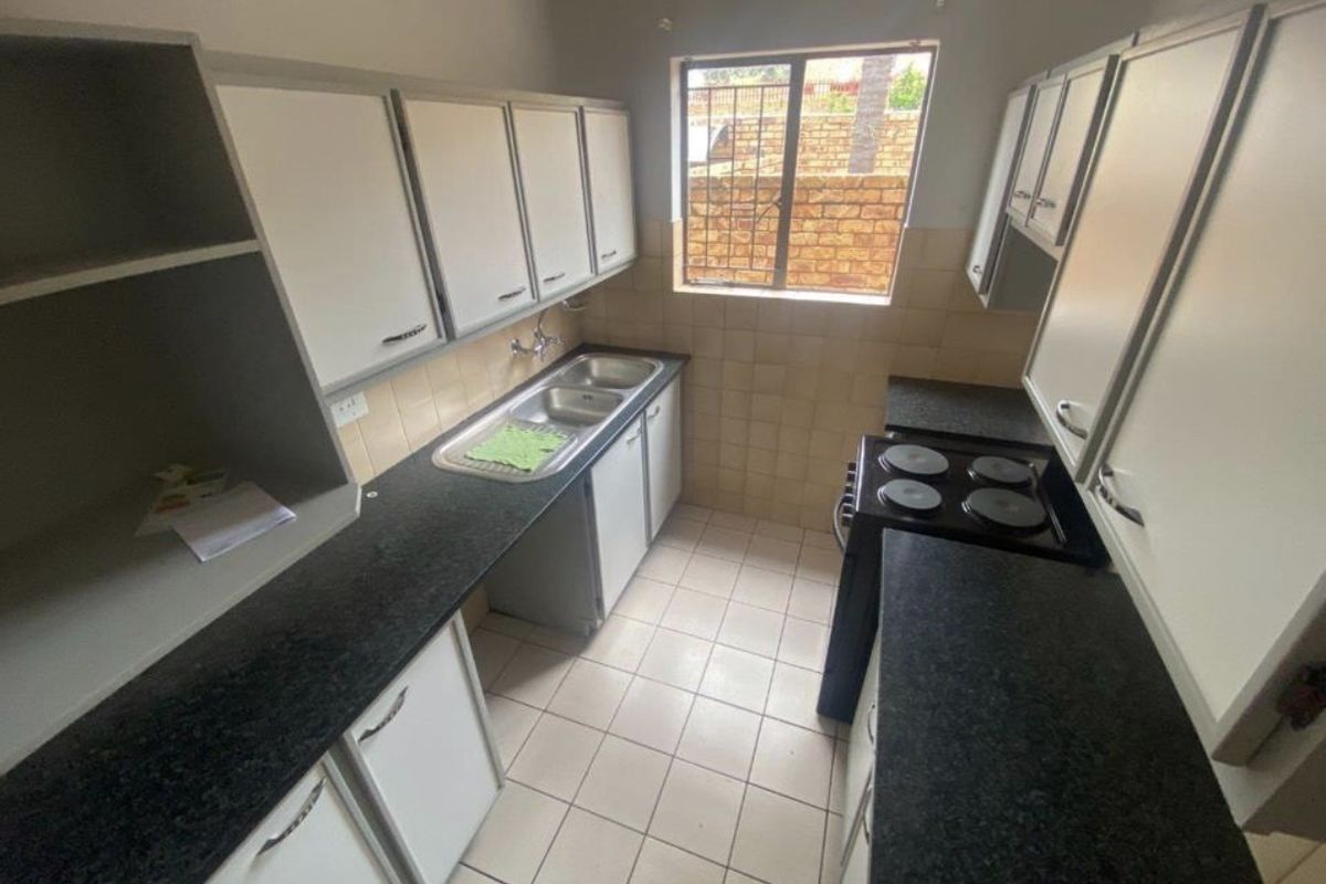 A functional kitchen featuring built-in cabinetry, granite countertops, a double basin sink, and a tiled backsplash with a window overlooking the exterior.