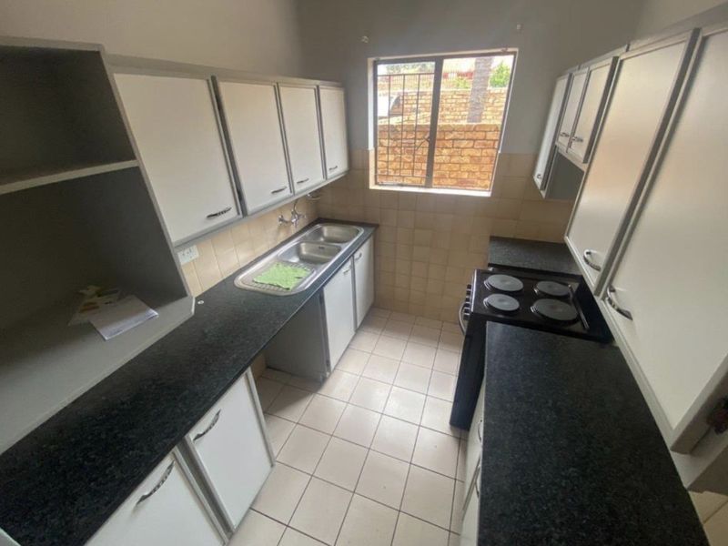 A functional kitchen featuring built-in cabinetry, granite countertops, a double basin sink, and a tiled backsplash with a window overlooking the exterior.