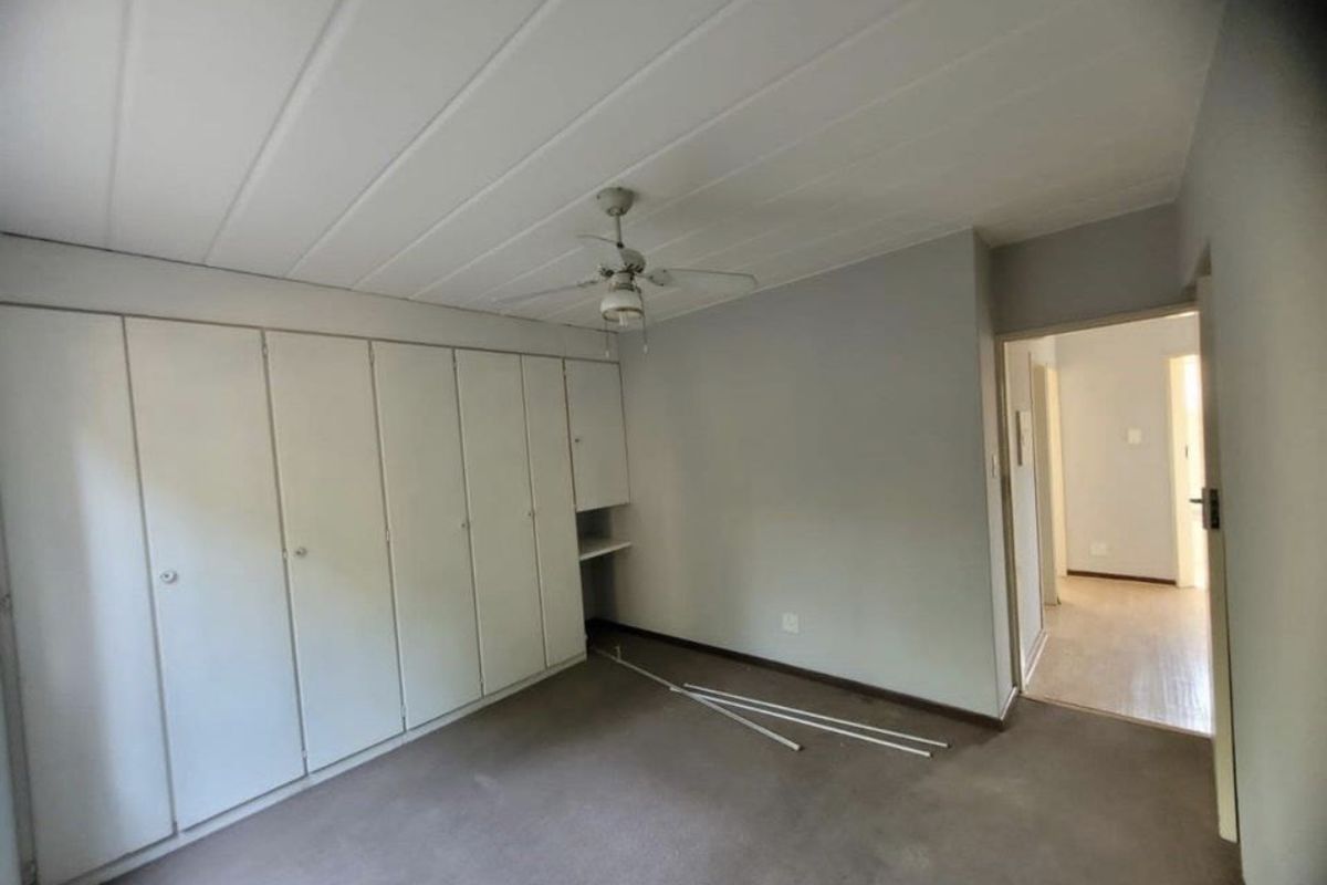 A vacant bedroom featuring extensive built-in cupboard storage, a ceiling fan, and a panelled ceiling, requiring cosmetic updates to the flooring and finishes.