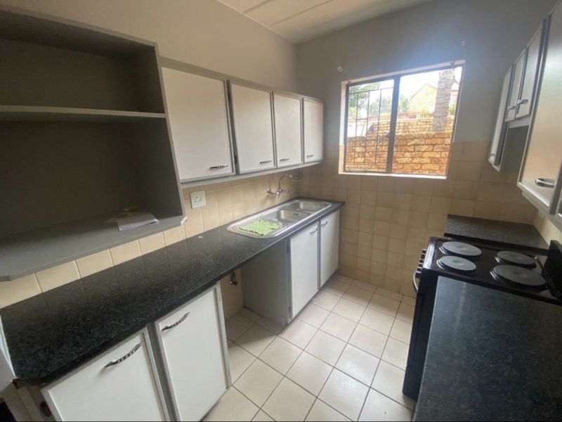 A functional kitchen featuring granite countertops, double basin sink, ample built-in cabinetry, and tiled flooring, offering a clean space ready for modernization.