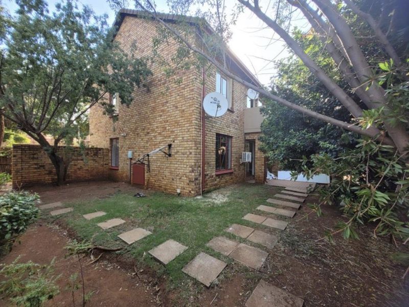 Rear view of a face brick apartment building featuring a private garden area with a paved walkway and established trees.