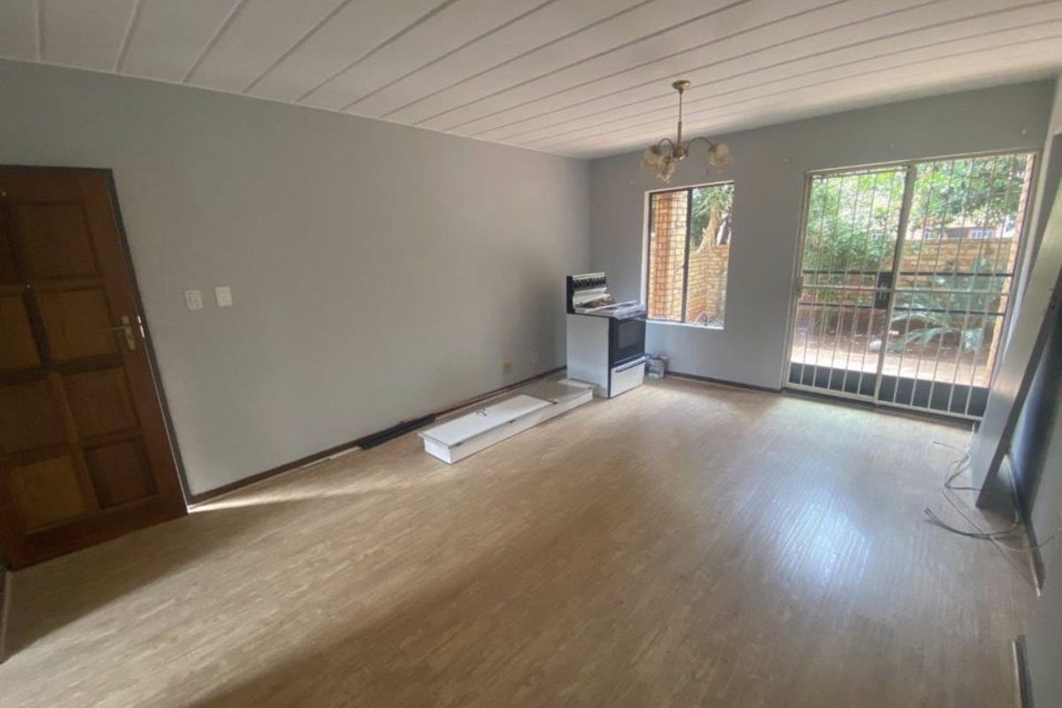 An empty living room featuring laminate flooring, ceiling panels, and a sliding glass door with security gate leading to the exterior.