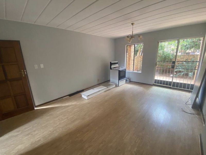 An empty living room featuring laminate flooring, ceiling panels, and a sliding glass door with security gate leading to the exterior.