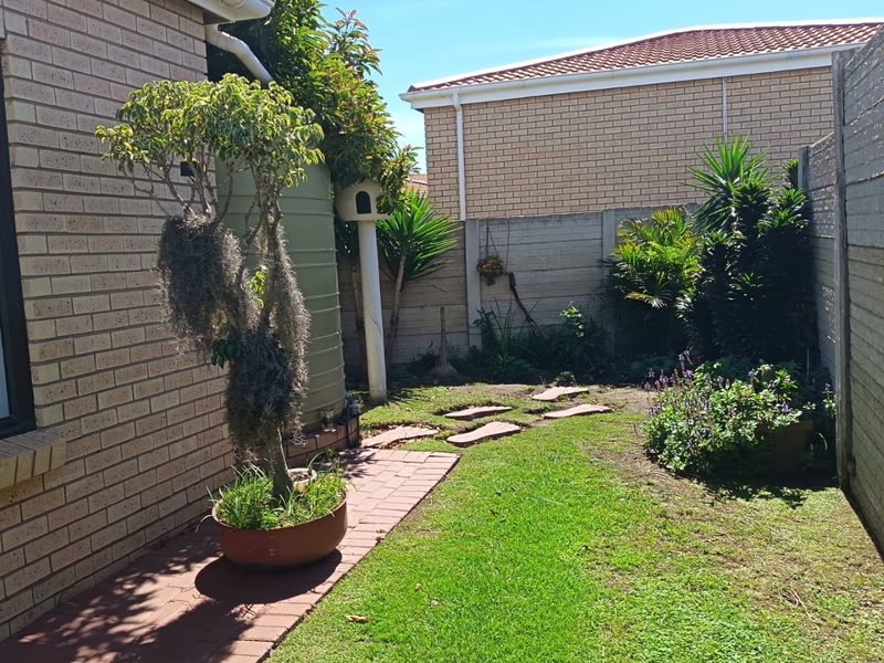 A private rear garden featuring a paved walkway, established landscaping, and a water tank, enclosed by a secure boundary wall.