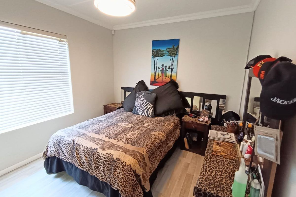 A well-maintained bedroom featuring light-toned laminate flooring, neutral wall finishes, and venetian blinds, providing a clean and functional living space.