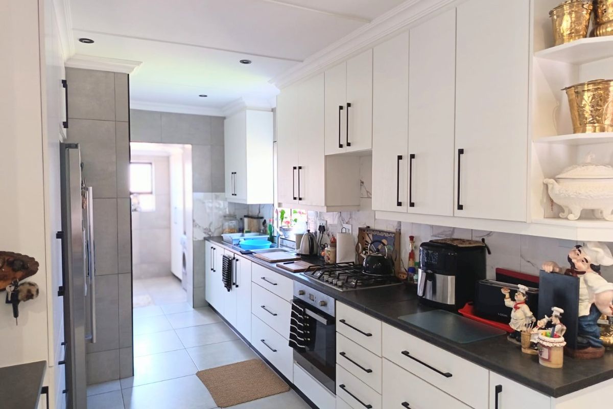Modern kitchen featuring white cabinetry, dark stone countertops, gas hob, built-in oven, and marble-look splashback, with an adjacent scullery area.