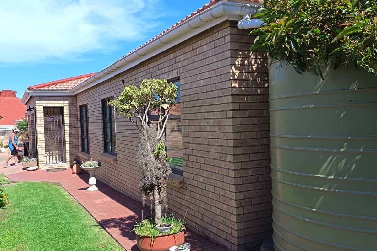 Rear exterior view of the townhouse featuring face brick walls, terracotta roof tiles, a paved walkway, and a large rainwater tank.
