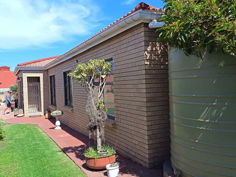 Rear exterior view of the townhouse featuring face brick walls, terracotta roof tiles, a paved walkway, and a large rainwater tank.