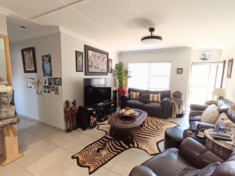 A well-lit living room featuring neutral tiled flooring, ceiling fan, and large windows with blinds, offering a comfortable and functional living space.
