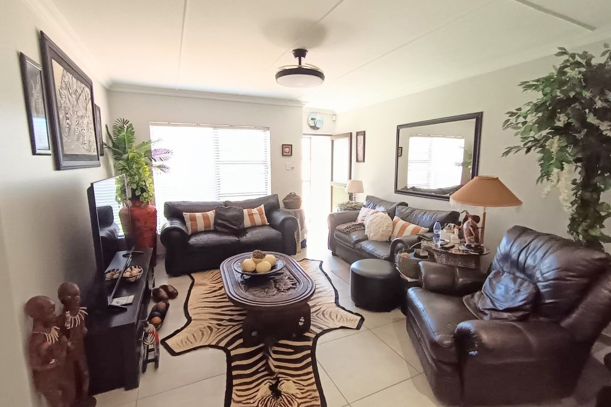 A comfortable living room featuring tiled flooring, a ceiling fan, and natural light through venetian blinds.
