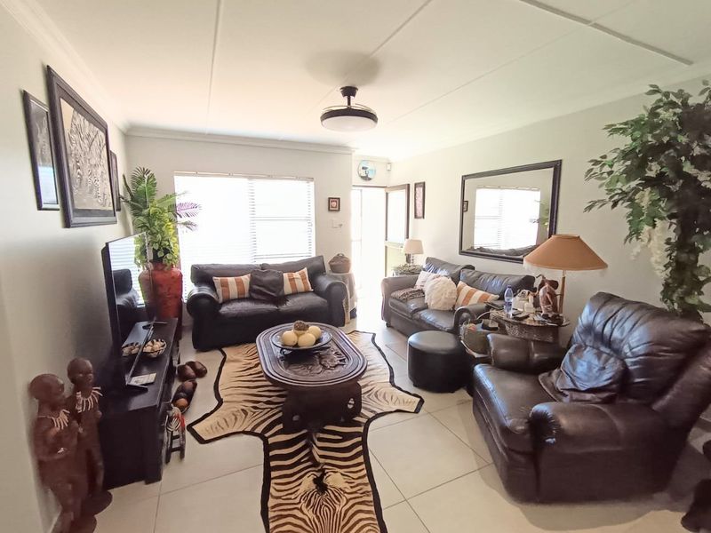 A comfortable living room featuring tiled flooring, a ceiling fan, and natural light through venetian blinds.