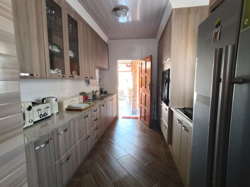 A functional galley-style kitchen featuring wood-look cabinetry, built-in oven, gas hob, and direct access to an outdoor patio area.