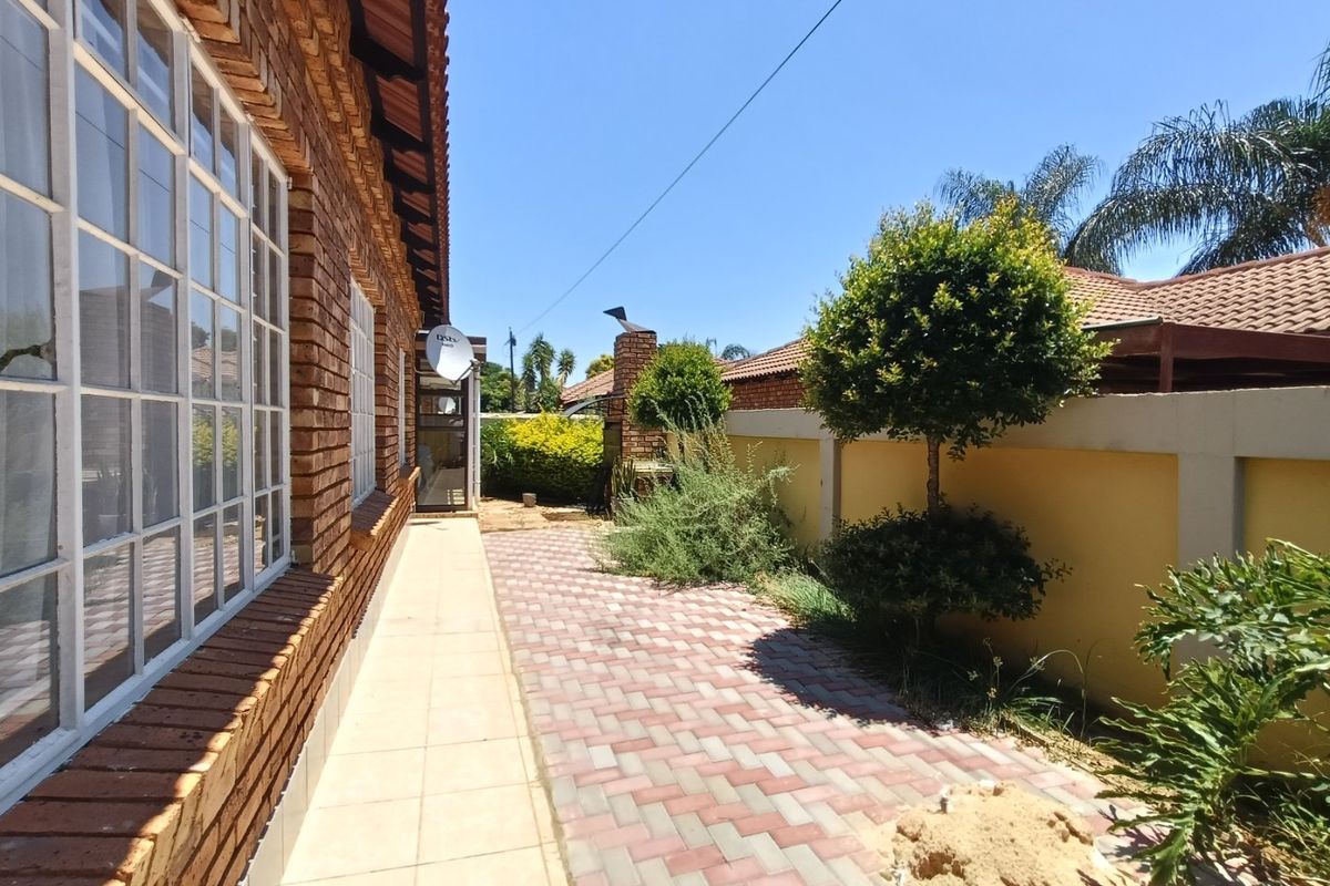 Rear exterior view of the townhouse featuring a brick facade, paved walkway, tiled patio area, and a built-in braai against the boundary wall.