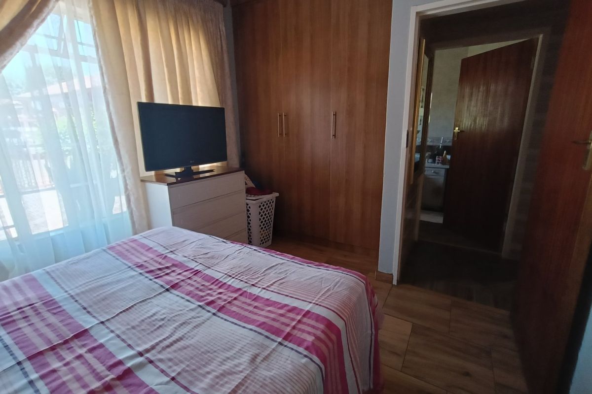 A bedroom featuring built-in wooden cupboards, laminate flooring, and an adjoining doorway leading to an en-suite bathroom.