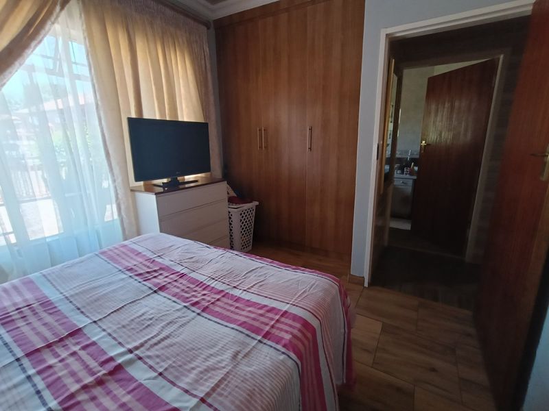A bedroom featuring built-in wooden cupboards, laminate flooring, and an adjoining doorway leading to an en-suite bathroom.